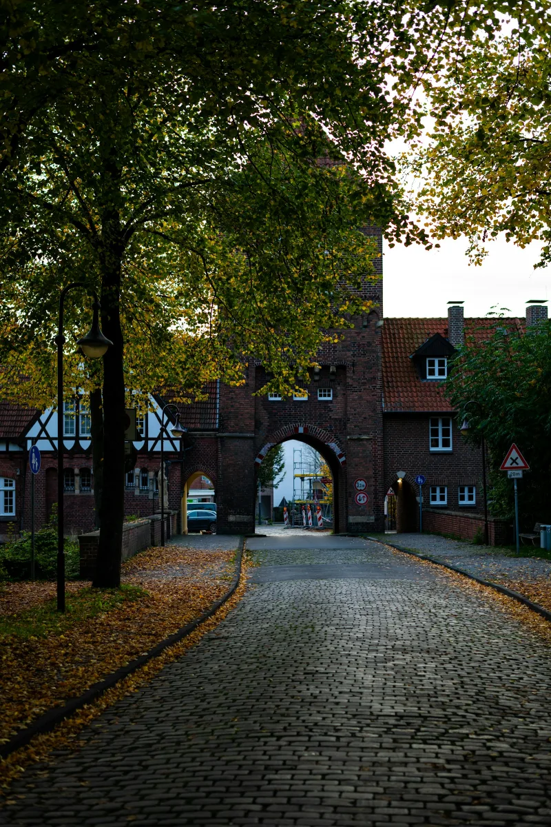 Historic brick gatehouse with cobblestone street and autumn leaves